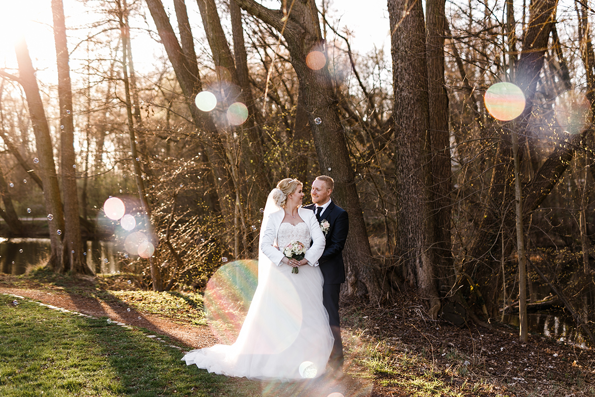 Idee Pose Hochzeitsfoto Brautpaar im Wald und Kleidung Winterhochzeit mit weißer Bolero-Jacke Braut und schwarzem Anzug Bräutigam - Hochzeitsfotografin aus Berlin hat Winterhochzeit am Wasser in Brandenburg im Landgasthof Zum Mühlenteich begleitet © www.hochzeitslicht.de