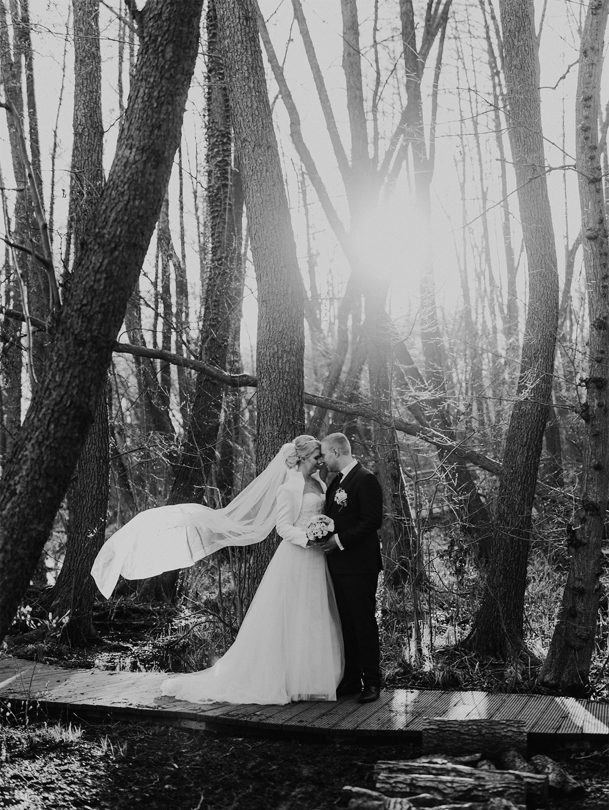 Inspiration Brautpaar Foto Posing auf Steg im Wald bei Landhochzeit Hochzeitskleid Braut aus Tüll und Spitze ohne Träger mit Schleppe und weißer Bolero-Jacke und wehendem Schleier - Hochzeitsfotografin aus Berlin hat Winterhochzeit am Wasser in Brandenburg im Landgasthof Zum Mühlenteich begleitet © www.hochzeitslicht.de