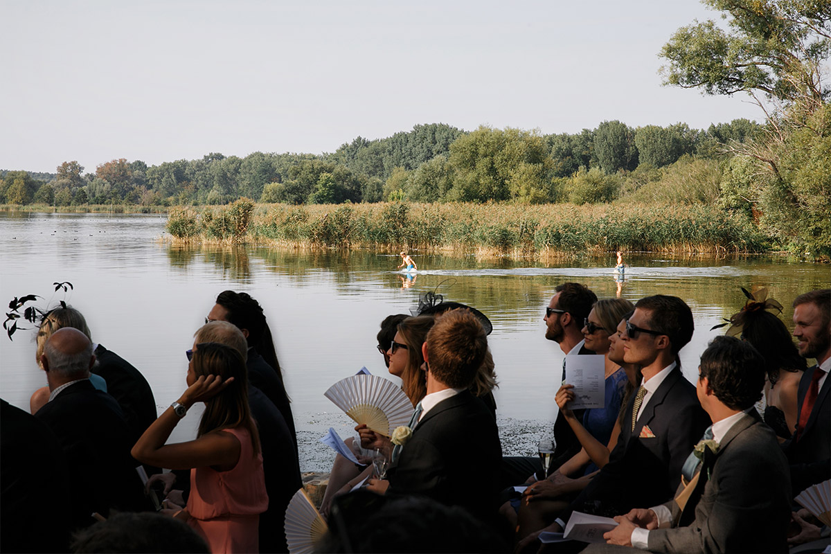 Hochzeitsreportagefoto von Gästen bei freier Trauung am See auf Gut Schloss Golm an heißem Sommertag, die badende Kinder beobachten © Hochzeitsfotograf Berlin www.hochzeitslicht.de