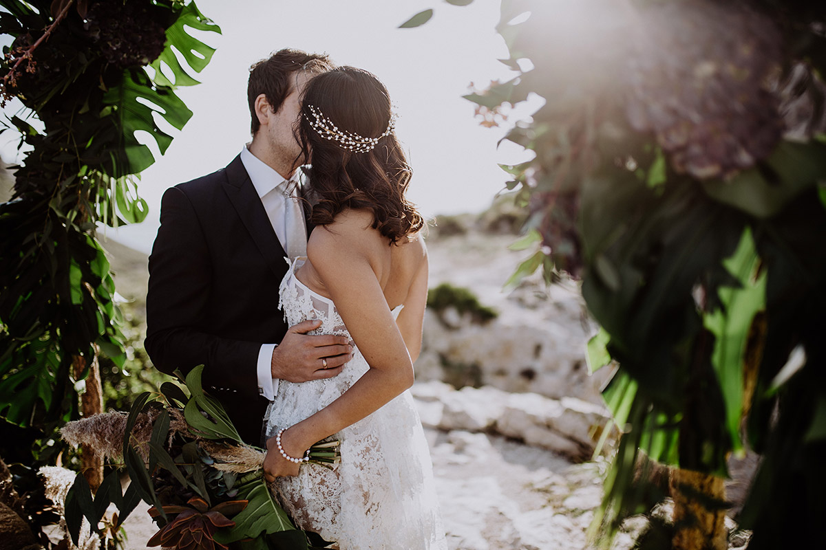 Brautpaarfoto unter Blumenbogen mit Monsterablättern von Hochzeitsfotograf