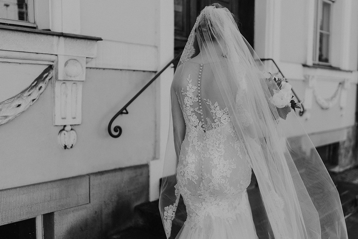 schwarz-weiß Hochzeitsfoto Braut von hinten Pronovias Brautkleid mit tiefem Rückenausschnitt und Spitze im Meerjungfrauenschnitt - Schloss Glienicke Hochzeitsfotograf Potsdam © www.hochzeitslicht.de