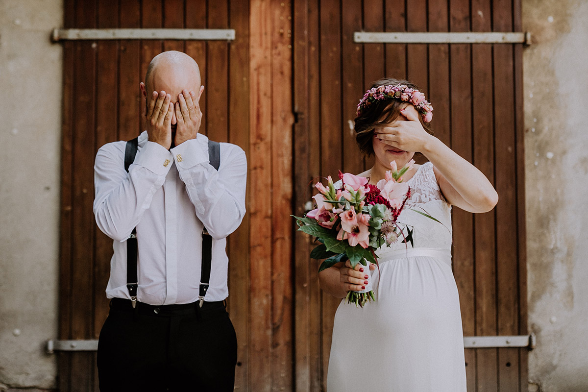 Idee Hochzeitsfoto First Look Brautpaar heiraten mit Babybauch, Bräutigam mit schwarzer Hose und Hosenträgern, Braut schwanger mit Brautstrauß aus rosa Sommerblumen, rosa Blumenkranz, Hochzeitskleid mit Spitze oben und weißem Gürtel - Hochzeitsfotograf Standesamt Rathaus Schöneberg © www.hochzeitslicht.de