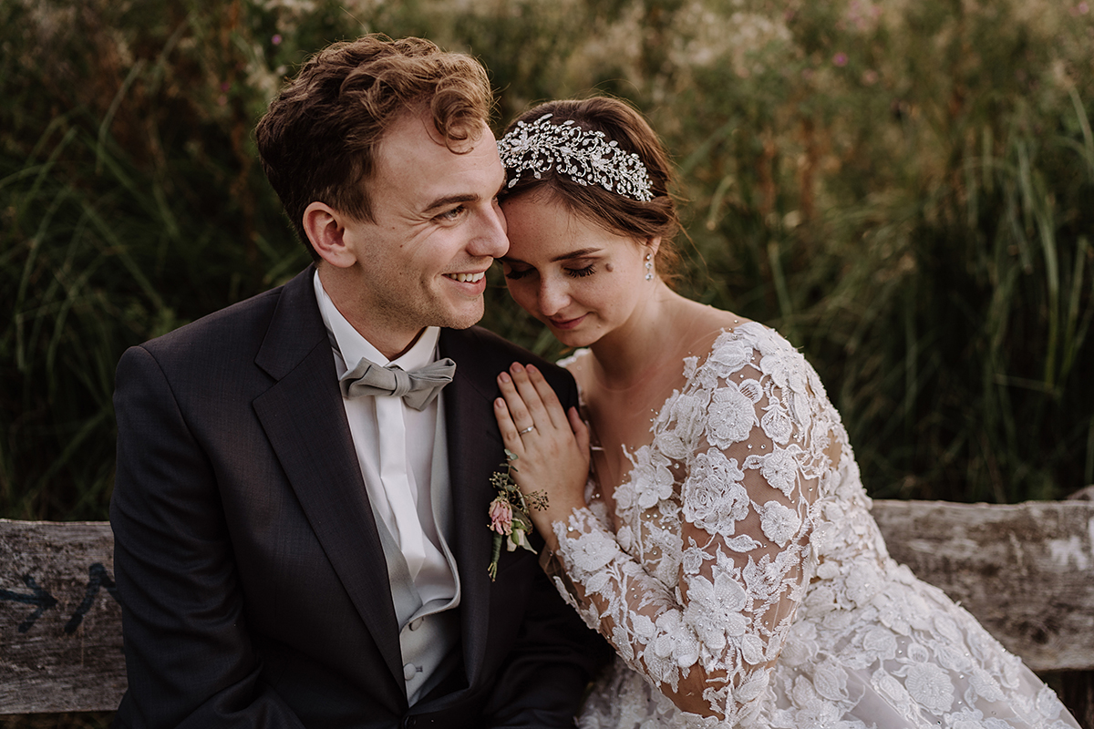 natürliches Hochzeitsfoto Braut und Bräutigam auf Bank in Natur - Landgut Stober Boho Hochzeit mit Alpaka von Hochzeitsfotografin Brandenburg © www.hochzeitslicht.de