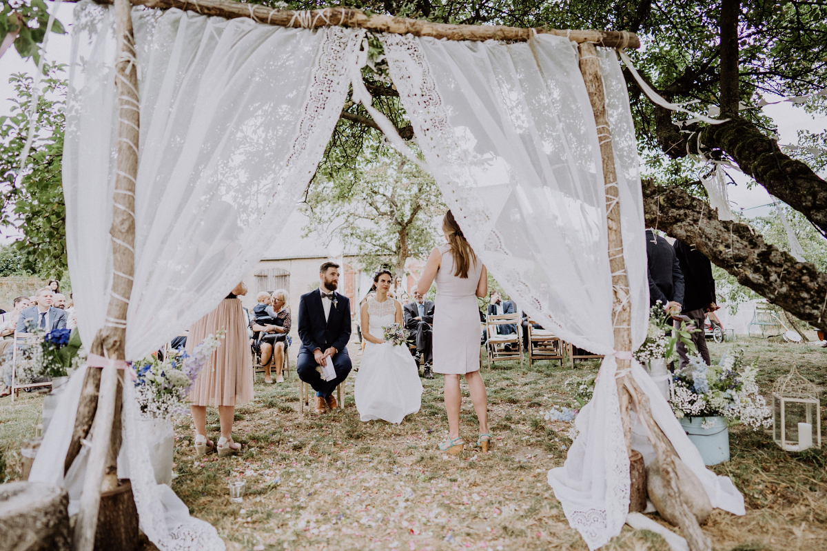 Hochzeitsfoto freie Trauung Bohohochzeit Traubogen Äste und weiße Spitze - Boho-Scheunenhochzeit in Brandenburg im Schmetterlingsgarten mit Hochzeitsfotografin aus Berlin © www.hochzeitslicht.de