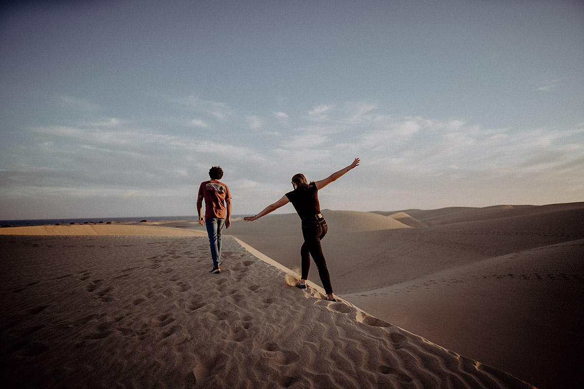 engagement photographer captures couple from behind walking along the beach in Gran Canaria