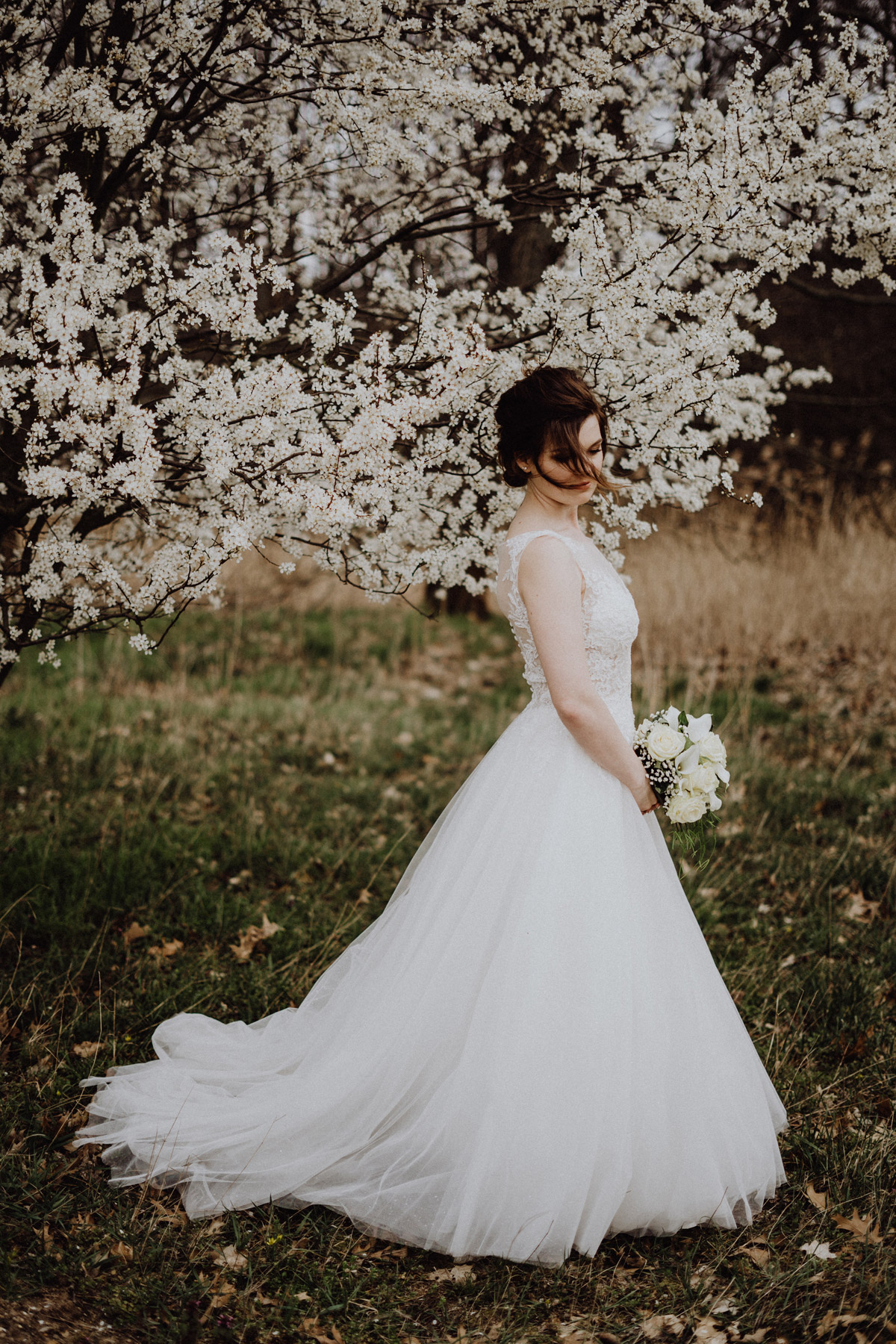 Braut Fotoshooting Idee Wald, Braut steht mit weißem Brautstrauß verträumt unter blühendem Kirschbaum und Haare ihrer natürlichen Hochsteckfrisur wehen ihr locker in das Gesicht auf Corona Micro-Wedding in Springbachmühle von vintage Hochzeitsfotografin aus Berlin #hochzeitslicht © www.hochzeitslicht.de