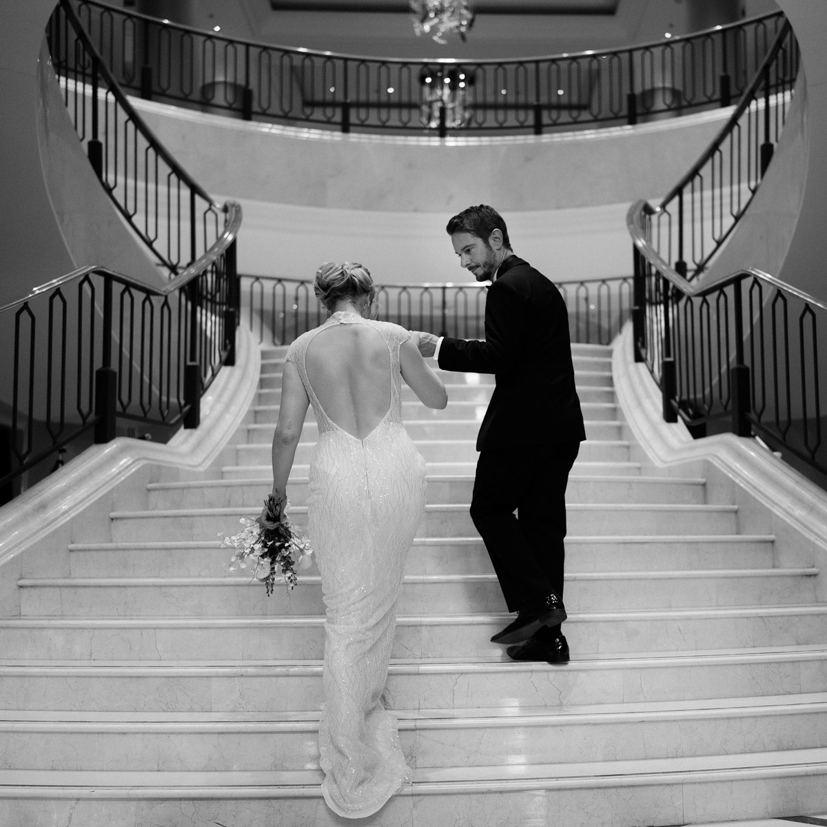 Hochzeitspaar von hinten geht Treppe nach oben. Originelles Hochzeitsfoto in Schwarz Weiß im The Ritz Carlton Berlin Hotel von #hochzeitslicht Hochzeitsfotograf © www.hochzeitslicht.de