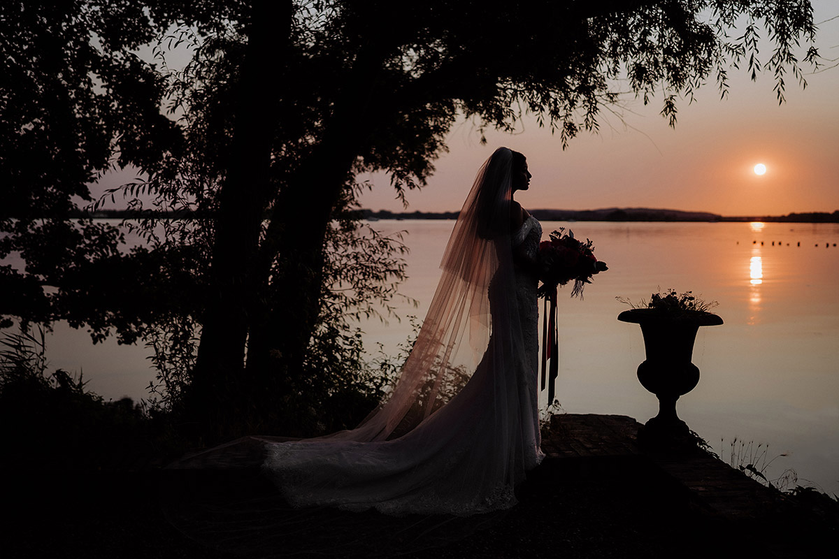 Hochzeitsfotografin aus Berlin in Hochzeitslocation Potsdam am Wasser im Gut Schloss Golm zeigt Braut im Sonnenuntergang als Silhouette © www.hochzeitslicht.de #hochzeitslicht