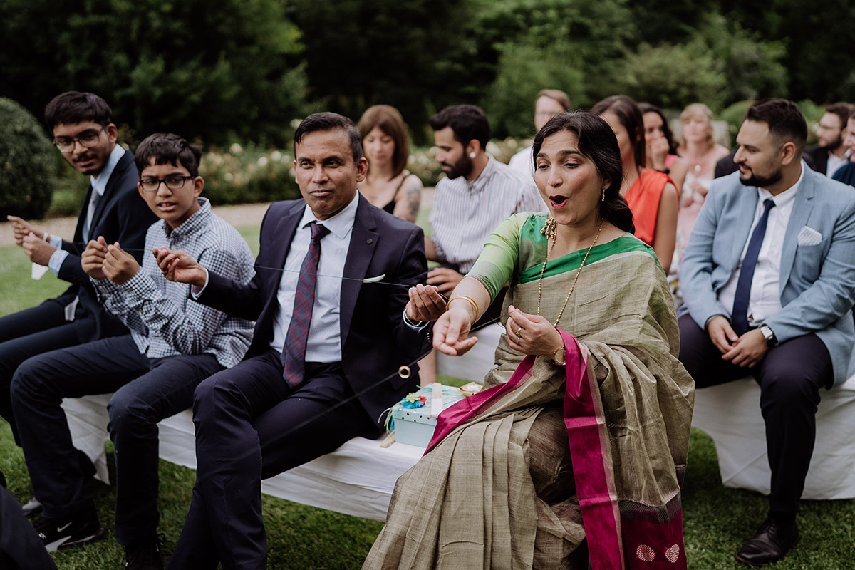 Ringe werden an Band von Gast zu Gast weitergereicht und mit guten Wünschen aufgeladen - Hochzeitsfotografin aus Berlin auf eleganter Gartenhochzeit in Hochzeitslocation Potsdam am Wasser im Gut Schloss Golm während Corona Pandemie © www.hochzeitslicht.de #hochzeitslicht