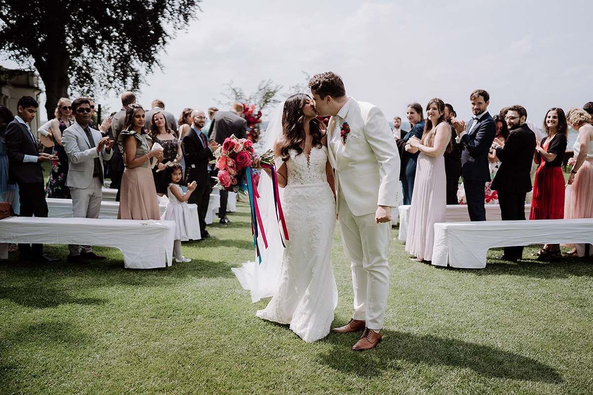 Hochzeitsfoto küssendes Brautpaar bei Auszug freie Trauung - Hochzeitsfotografin aus Berlin auf eleganter Gartenhochzeit in Hochzeitslocation Potsdam am Wasser im Gut Schloss Golm während Corona Pandemie © www.hochzeitslicht.de #hochzeitslicht