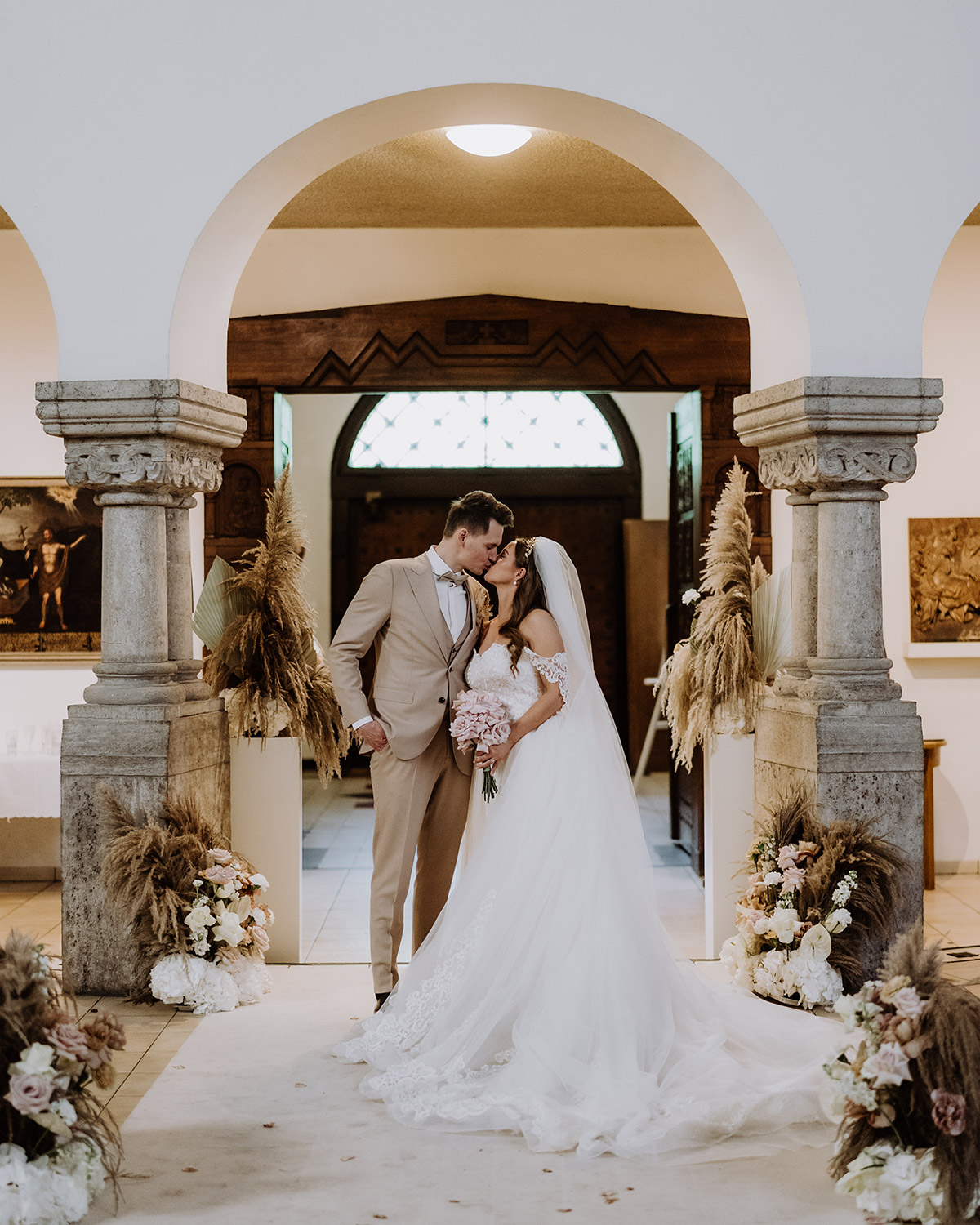 Boho Hochzeit Kirchendeko: Die Hochzeitsfotografin aus Berlin hat im Brautpaar Fotoshooting die schönsten Ideen und Blickwinkel für die Deko aus Pampasgras und Rouge-Akzenten gefunden. Der helle Anzug des Bräutigams und das Boho Hochzeitskleid machen den Look und diesen Hochzeitskuss perfekt. © www.hochzeitslicht.de #hochzeitslicht