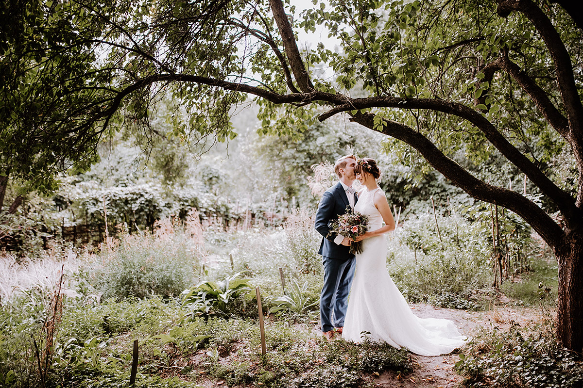 Hochzeitsfotograf der Villa Berlin Zehlendorf lässt Brautpaar unter Baum auf Gartenhochzeit küssen