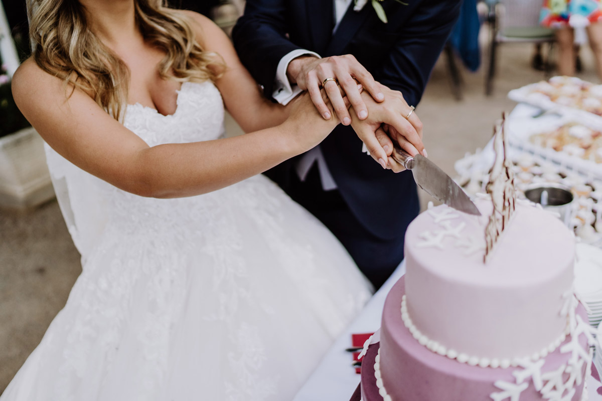Hände mit Eheringen beim Anschneiden der Hochzeitstorte