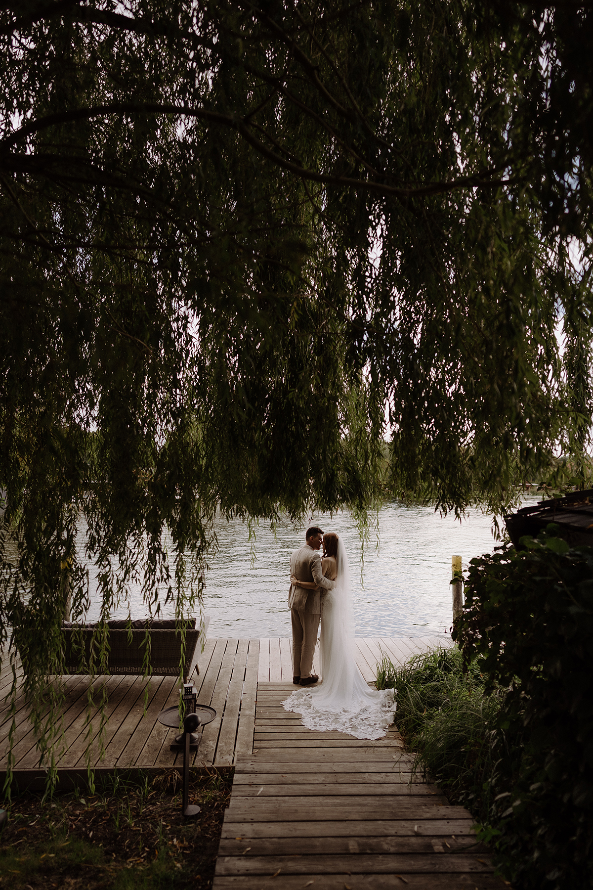 Remise am See Hochzeit: Heiraten im Boho Stil ist in dieser Hochzeitslocation in Potsdam am Wasser ideal möglich. Das Brautpaar von hinten steht im Hochzeitsfotoshooting ganz natürlich mit Blick auf den Schwielowsee. Entdecke diese Hochzeitsreportage im Blog!