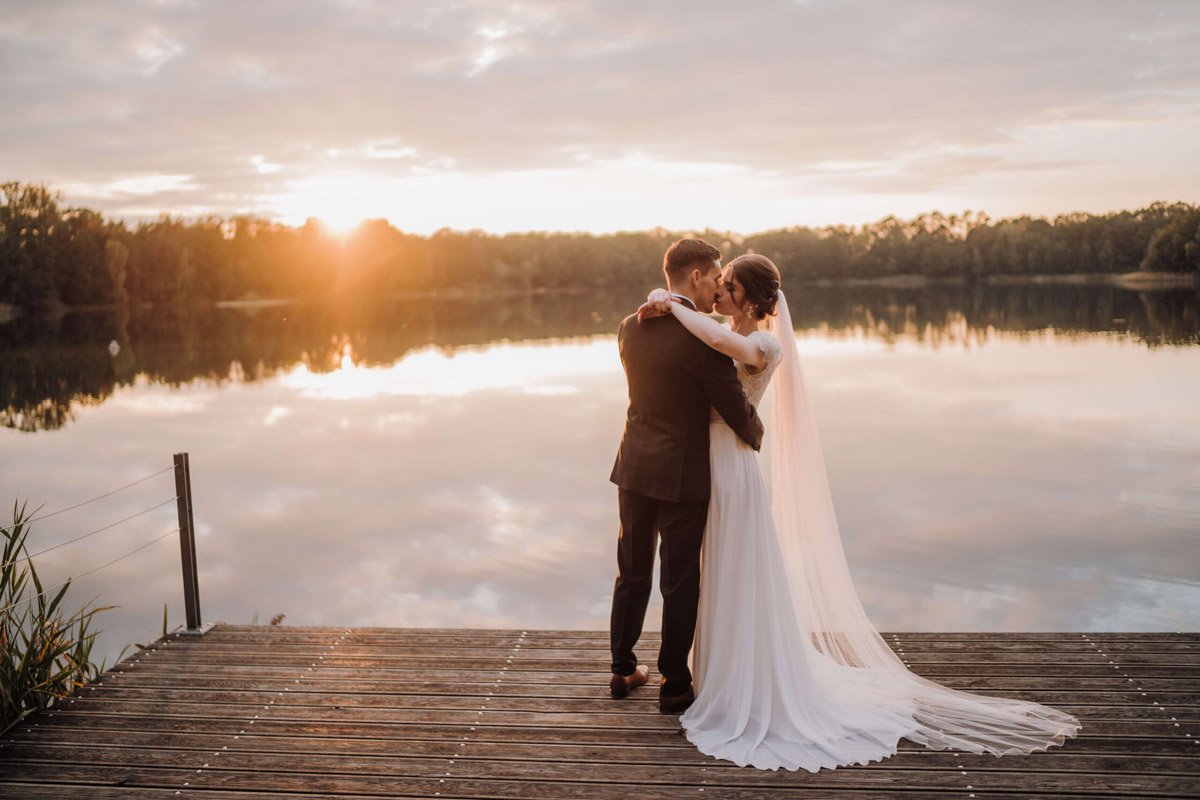 Hochzeit Seehaus Liebenberg Brautpaar küsst sich am Wasser bei Sonnenuntergang