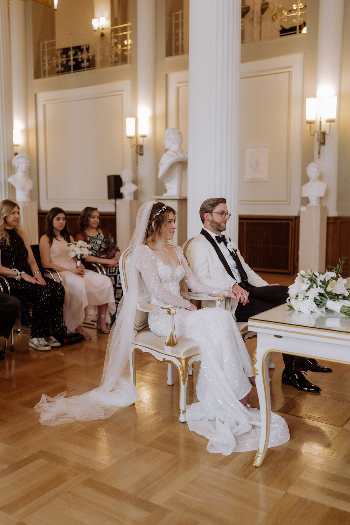 Standesamt Rotes Rathaus Hochzeit: Paar sitzt mit Gästen im Säulensaal