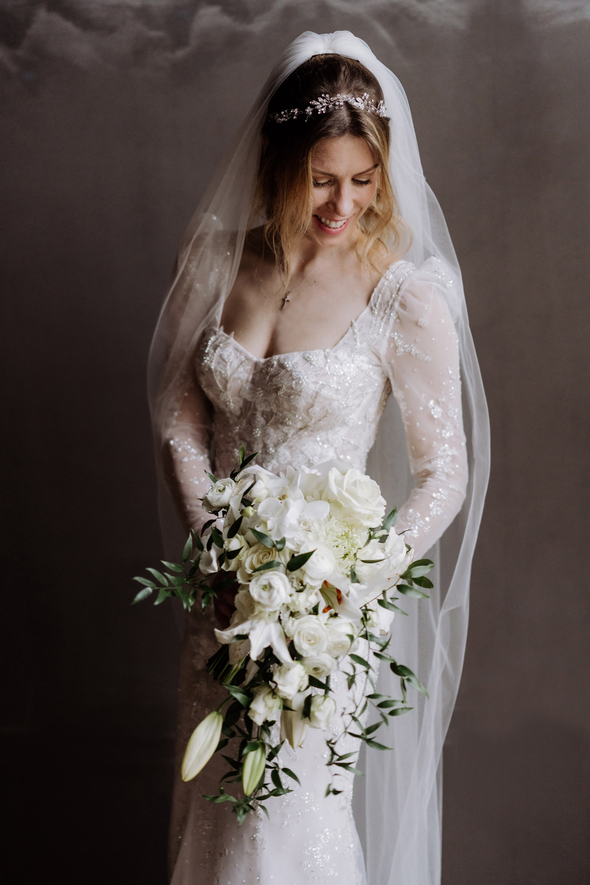 lachende Braut mit Schleier hält Brautstrauß in Tropfenform in Weiß und Grün mit Rosen, Ranunkeln und Lilien © www.hochzeitslicht.de #hochzeitslicht
